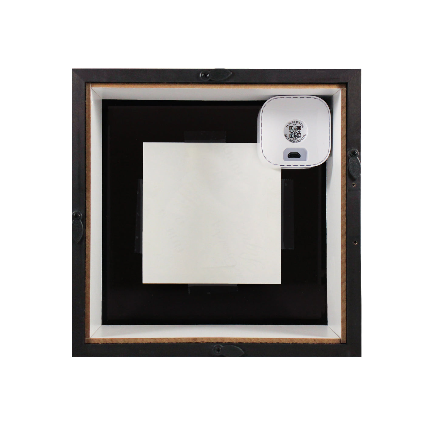 The back side of a picture frame with a piece of black film, the backside of a picture, and the back of a security camera visible.
